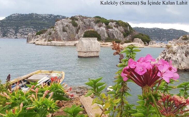 Kalek&ouml;y (Simena) kıyısında su i&ccedil;inde kalan antik lahit, &ouml;n planda &ccedil;i&ccedil;ekler ve eski bir sandal