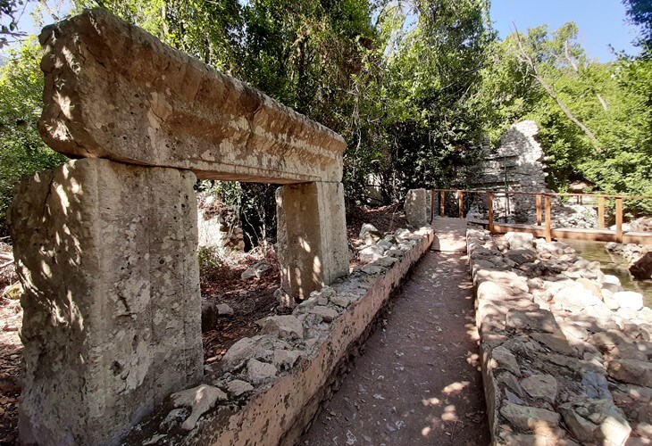Olympos Antik Kenti’nde taş bloklardan oluşan antik bir kapı ve ormanlık alanda uzanan yürüyüş yolu